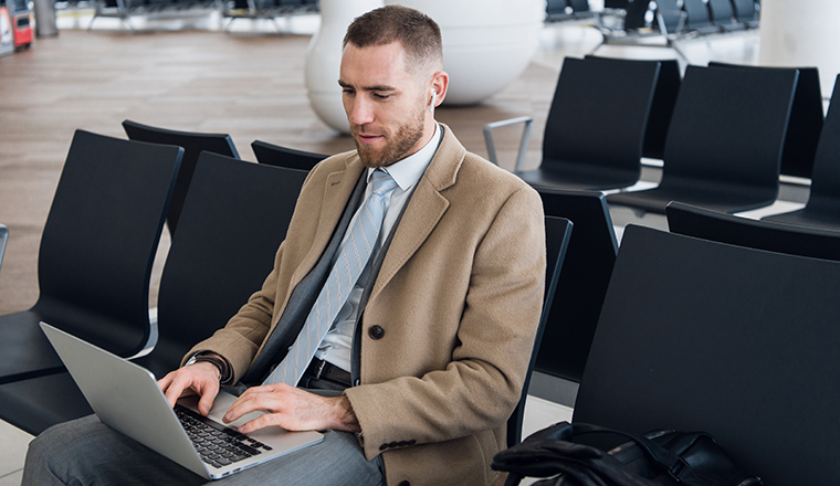 Always on the go. Portrait of handsome smiling businessman in formalwear holding a laptop with earphones while sitting in the airport.