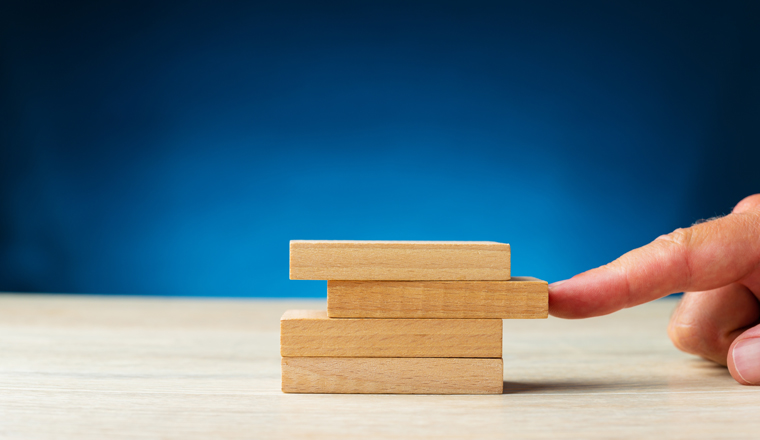 Male finger pushing a blank wooden peg second from the top in a stack of them in a conceptual image. Over blue background with copy space. 