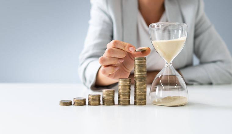 Close-up Of Businesswoman Holding Hourglass Near Stack Of Coins
