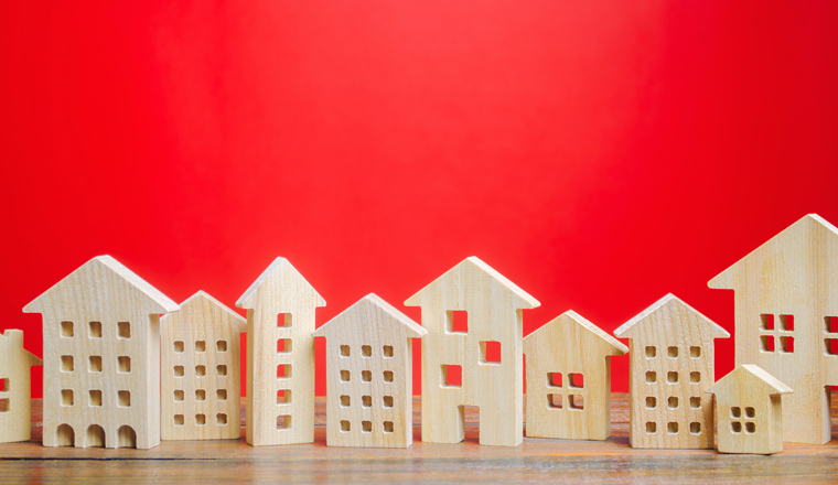 Miniature wooden houses on a red background. Real estate concept. City. Agglomeration and urbanization. Market Analytics. Demand for housing. Rising and falling home prices. Population. Copy space