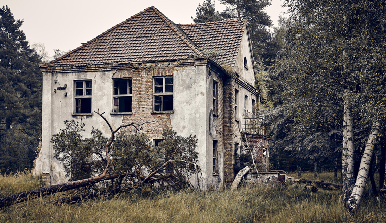 An old abandoned house on a grassy field surrounded by trees