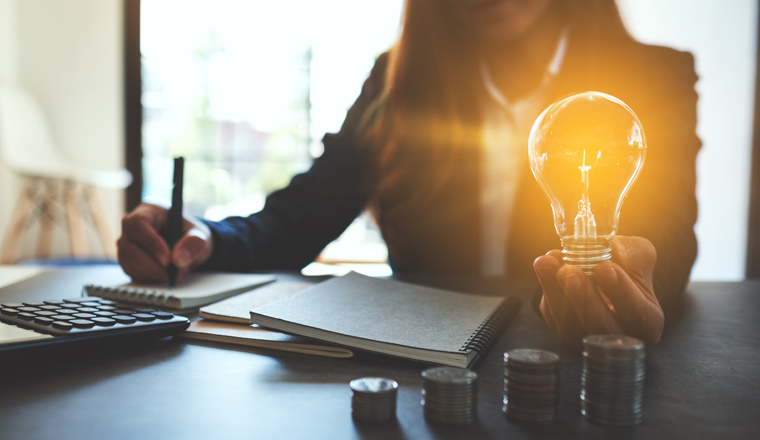 Businesswoman holding a lightbulb with coins stack on table, saving energy and money concept