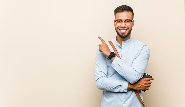 Young mixed race asian business man holding a phone smiling cheerfully pointing with forefinger away.