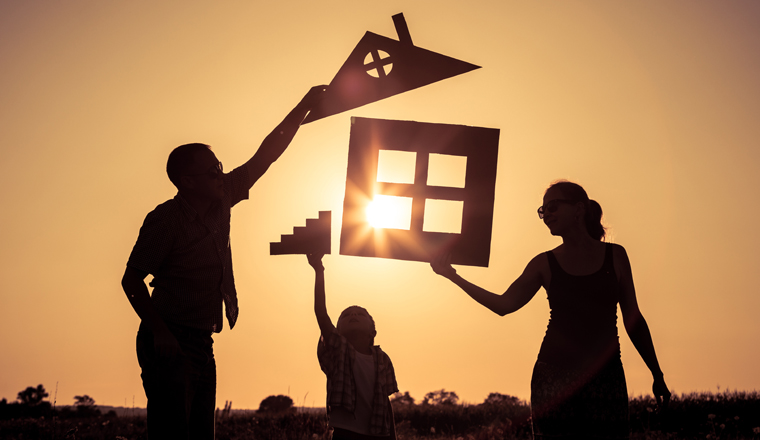 Happy family standing on the field at the sunset time. They build a house. Concept of friendly family.