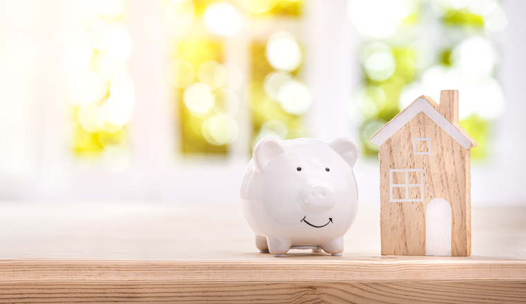 Piggy bank and model house on a bright interior room background