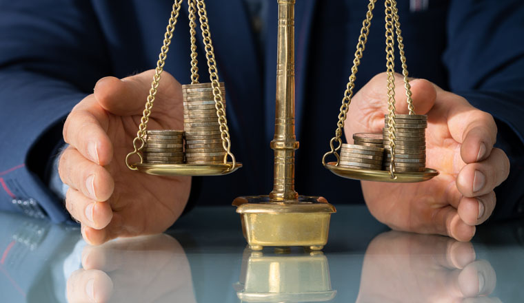 Close-up Of Lawyer's Hand Protecting Justice Scale With Coins At Table