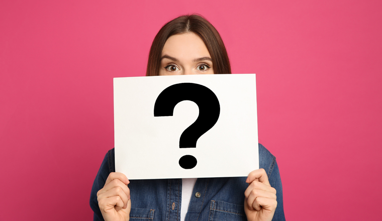 Emotional woman holding question mark sign on pink background