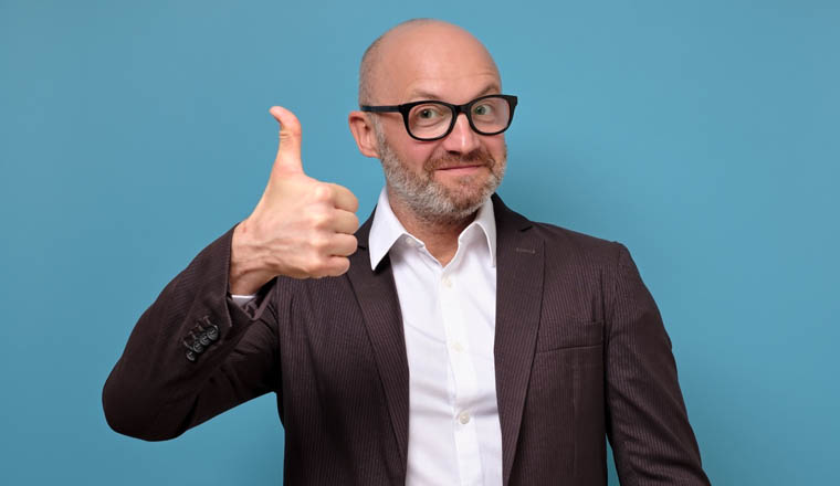 Handsome caucasian executive man in glasses in business suit gives the thumbs up