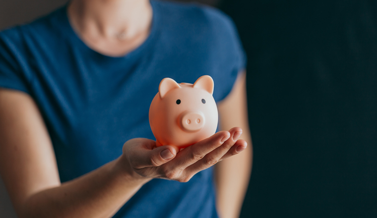 Woman holding a pink piggy bank, copy space next to her. Concept of saving money or savings