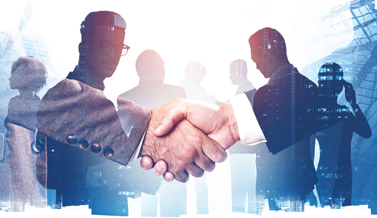 Two businessmen shaking hands in abstract city with double exposure of blurry diverse business people. Concept of partnership and teamwork. Toned image