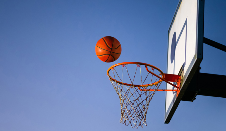 Street basketball ball falling into the hoop. Close up of orange ball above the hoop net with blue sky in the background. Concept of success, scoring points and winning. Copy space