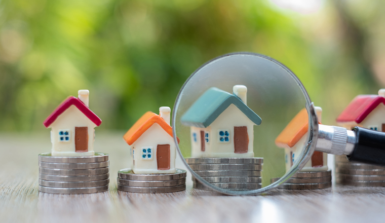 A magnifying glass placed near the house model placed on a pile of coins Search for houses, investment ideas, real estate, buy and sell houses, house selection, rental taxes, search