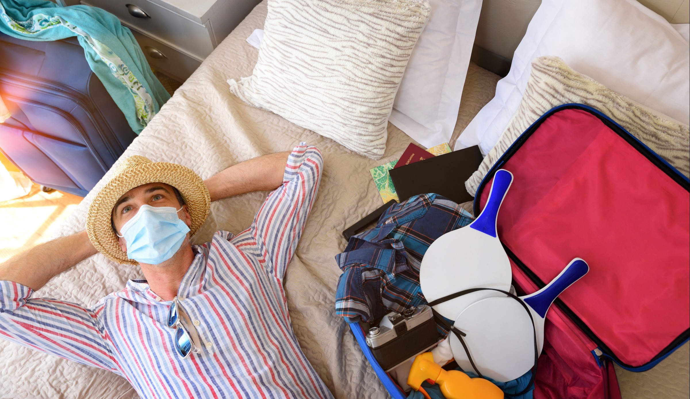 Man wishing to travel in coronavirus season lying in bed pensive with the suitcase prepared lying on the bed.