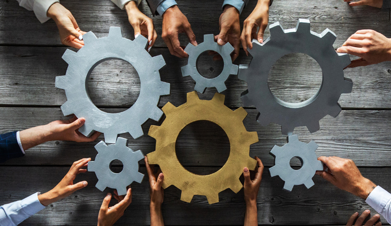 Group of business people joining together silver and golden colored gears on table at workplace top view