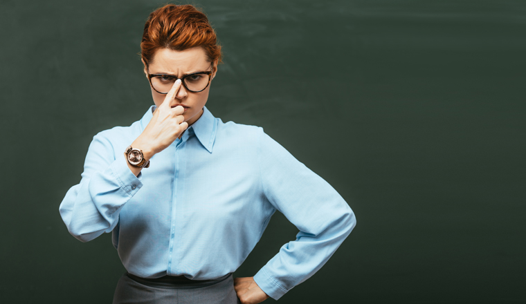 horizontal concept of strict teacher touching eyeglasses while standing with hand on hip near chalkboard