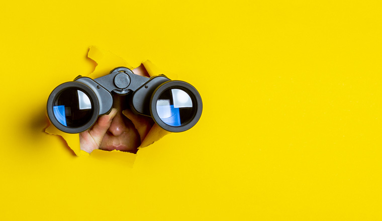 Female hand holds black binoculars on a yellow background. Journey, find and search concept. Banner