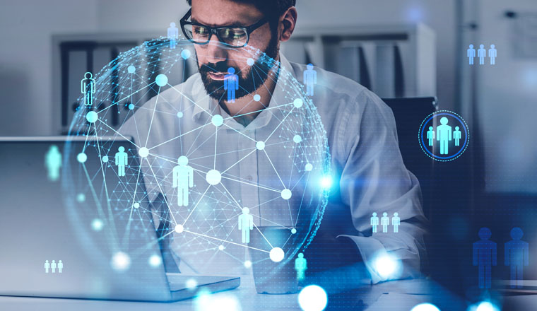 Young bearded businessman using laptop in blurry office with double exposure of social network interface. Concept of HR. Toned image