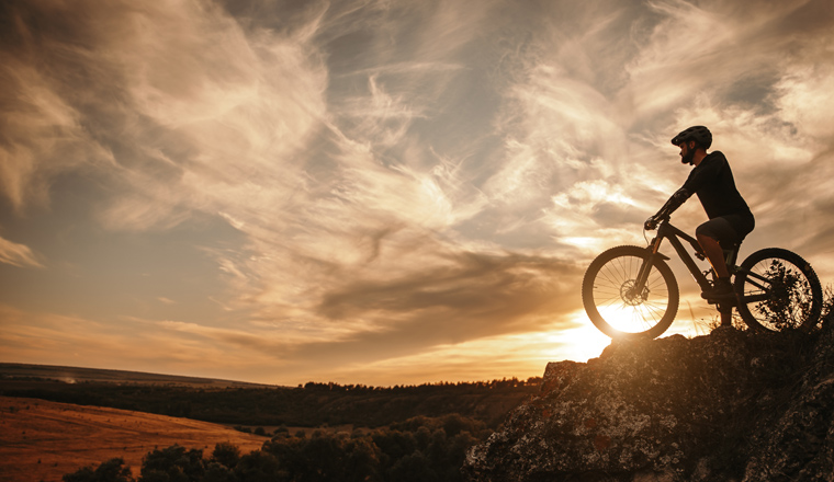 Side view of male cyclist in helmet sitting on mountain bicycle against cloudy sunset sky in countryside