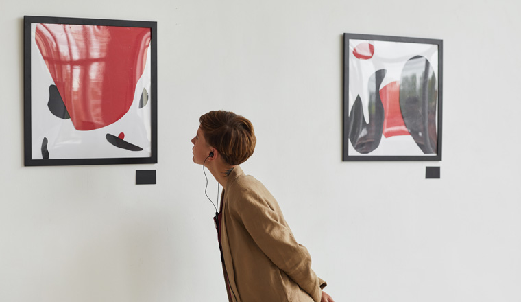 Wide angle portrait of tattooed young woman looking at paintings and listening to audio guide at modern art gallery exhibition, copy space