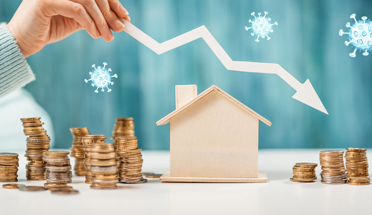 Woman holding an arrow down over model of the house and stack of coins. Concept of the crisis in the real estate market.