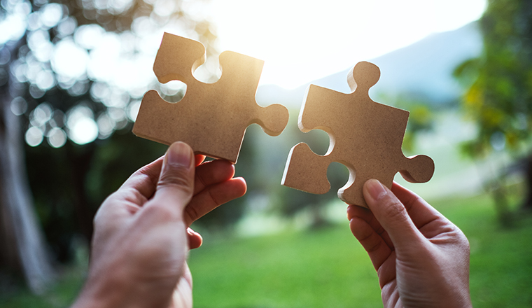 Closeup image of a woman holding and putting a piece of wooden jigsaw puzzle together in the outdoors