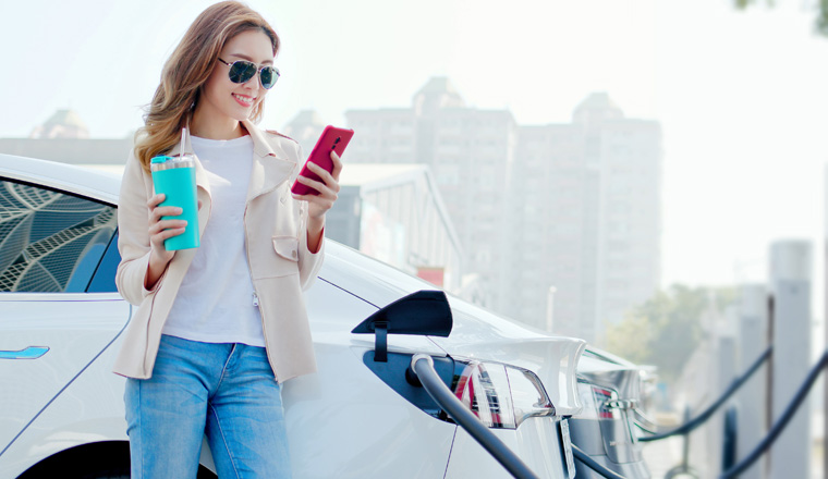asian woman use reusable eco-friendly ecological straw drink while using smart phone and waiting power supply connect to electric vehicles for charging the battery in car