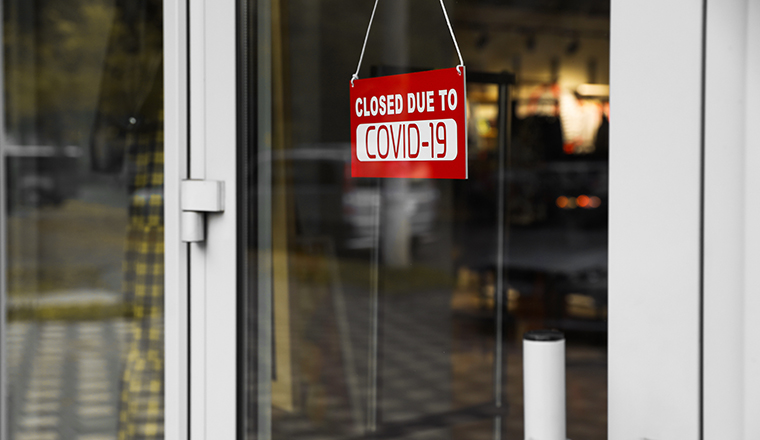 Red sign with words "Closed Covid-19" hanging on glass door