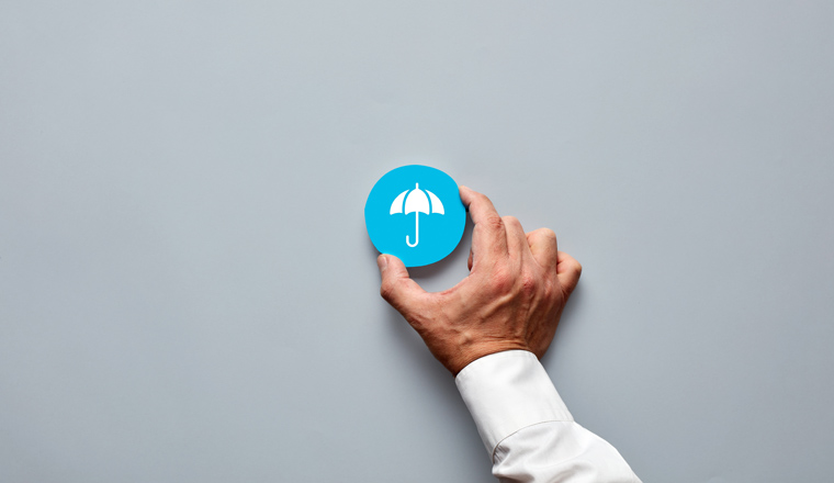 Businessman hand holding a blue badge with an umbrella icon representing insurance and protection.