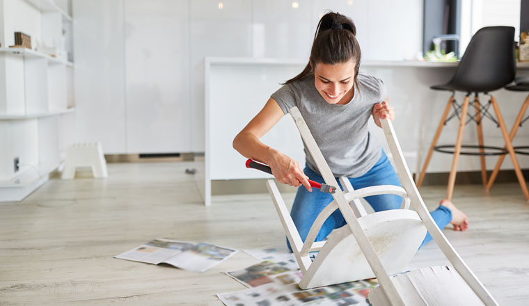 Woman as a handyman at home painting a chair or painting as upcycling