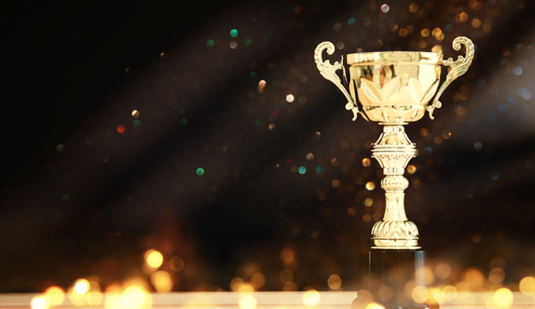 image of gold trophy over wooden table and dark background, with abstract shiny lights