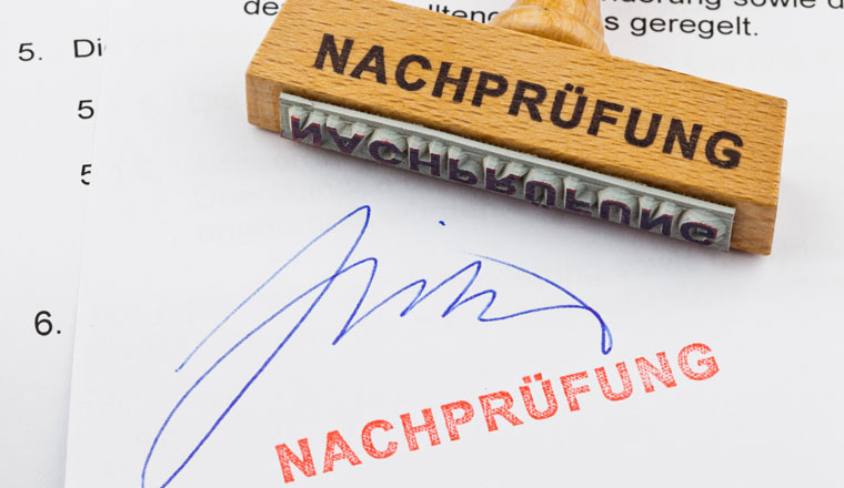 Ein Stempel aus Holz liegt auf einem Dokument. Deutsche Aufschrift Nachprüfung