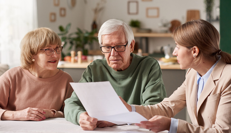 Senior couple sitting at the table and discussing documents with real estate agent they making a will