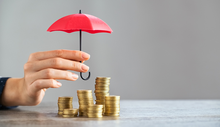 Young woman hand holding small red umbrella over pile of coins on table. Close up of stack of coins with female hands holding umbrella for protection. Financial safety and investment concept.  