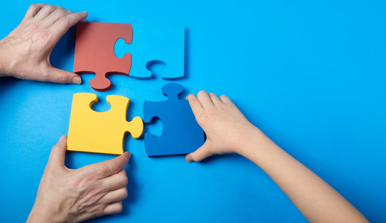 Top view hands of a autistic child and father arranging color puzzle symbol of awareness for autism spectrum disorder. Autism Awareness Day or month