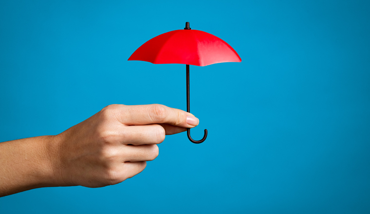 Female hand with small red umbrella isolated on blue background. Close up of woman hand holding mini umbrella against blue wall with copy space. Insurance, protection and security concept.