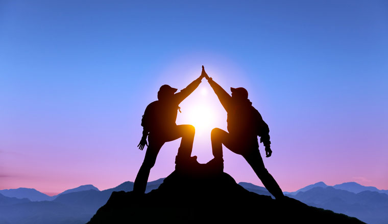The Silhouette of two man with success gesture standing on the top of mountain 