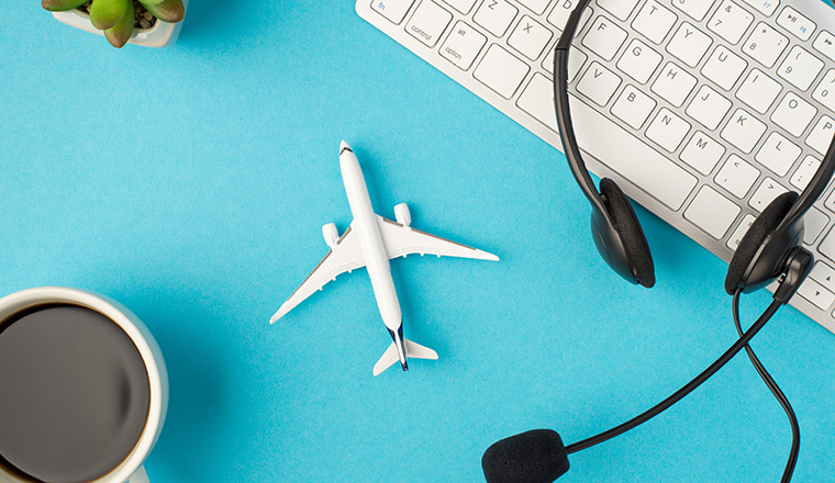 Top view photo of black headphones with microphone on white keyboard plant cup of coffee and plane model in the middle on isolated pastel blue background