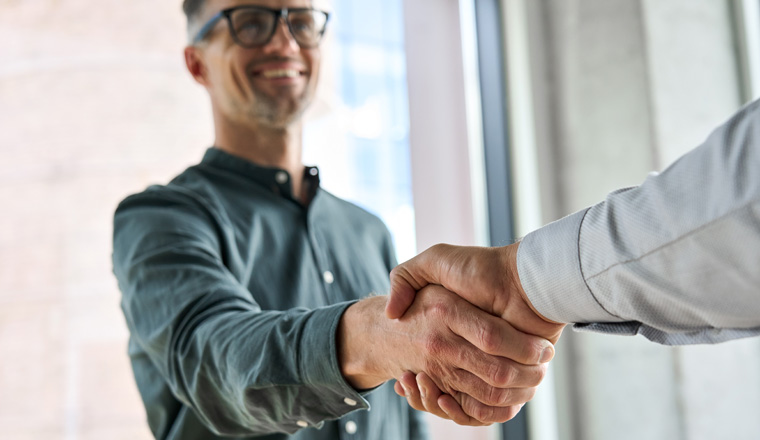 Two happy diverse professional business men executive leaders shaking hands at office meeting. Smiling businessman standing greeting partner with handshake. Leadership, trust, partnership concept.