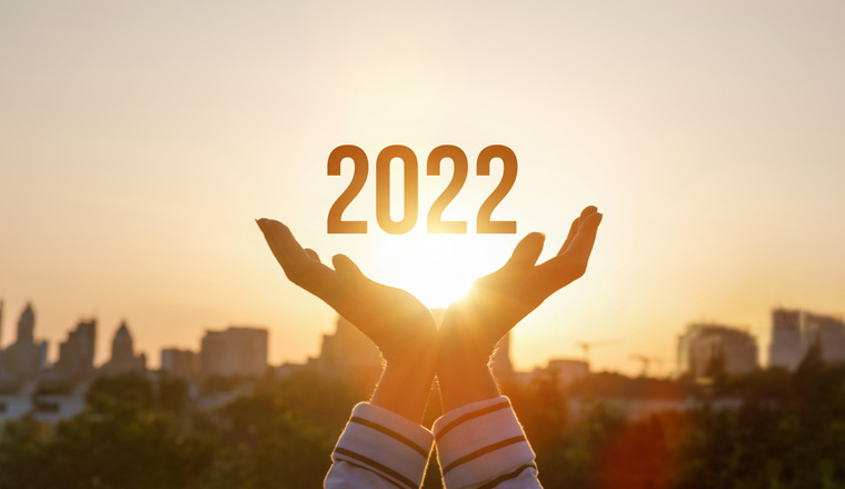 2022 is supported by woman hands on the background of a sunny sunset.