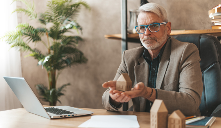 The house is inherited. Senior man holding a model house in his hands. Financial advice, real estate insurance.