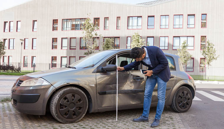 Side view of brunette male auto insurance adjuster inspecting a vehicle that has been in an accident wreck, wearing jeans and jacket, assesses the damage to the car. Outdoor shot.