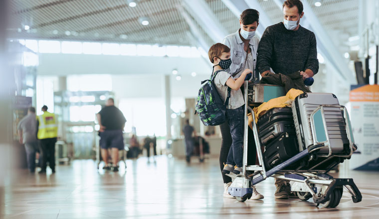 Couple with son walking at airport pushing luggage trolley. Family at airport traveling during pandemic.