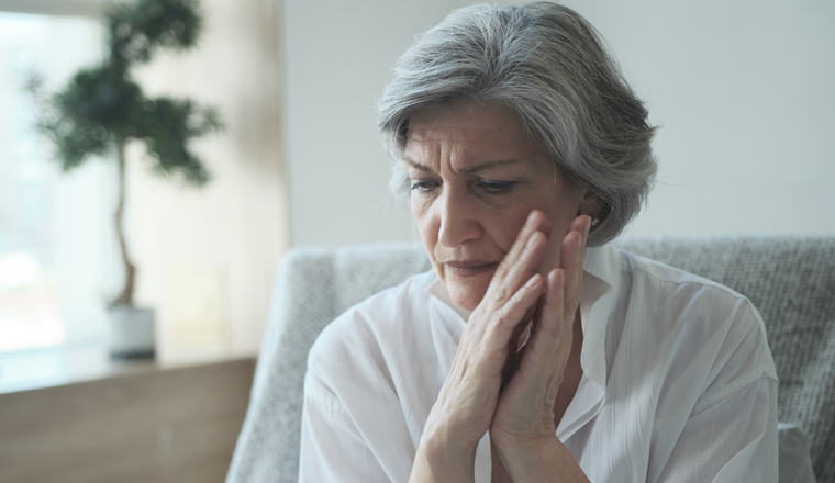 Elderly senior woman massaging her temples to reduce her headache. Older lady feeling scared, anxious, and thinking of sickness or mental health while suffering from a severe migraine or memory loss.