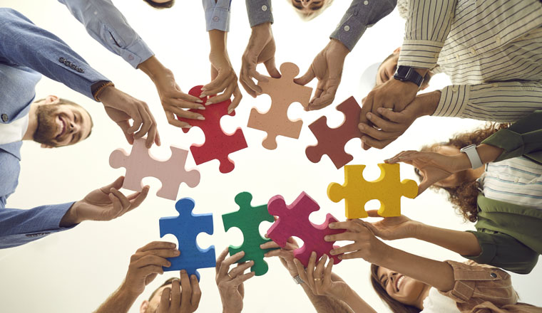 Group of young and mature people making circle of colorful jigsaw puzzle parts, low angle shot from below. Happy business team enjoying teamwork, finding professional solution, starting new enterprise