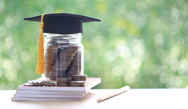 Graduation hat on coins money in the glass bottle on natural green background, Saving money for education concept