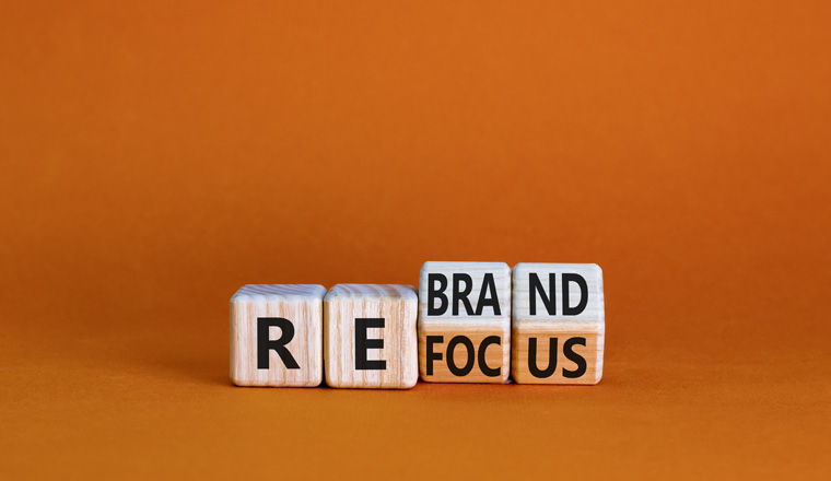 Refocus and rebrand symbol. Turned cubes and changed the word 'refocus' to 'rebrand'. Beautiful orange table, orange background. Business, refocus and rebrand concept. Copy space.