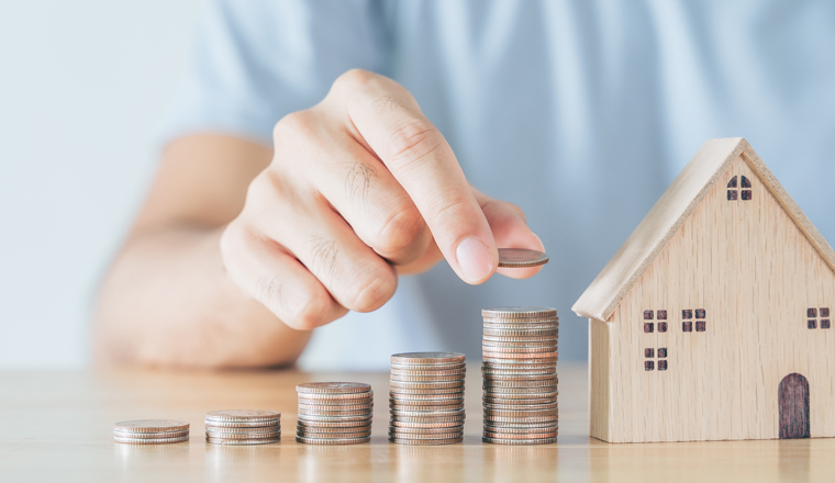 Man hand put coin on coins stack with wooden house on wood table. saving money for buying house, financial plan home loan concept.