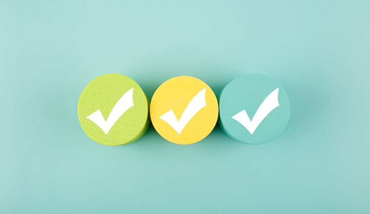 Three white checkmarks on multicolored toy circles in a row in the middle on bright aqua blue background. Concept of questionary, checklist, to do list, planning, business or verification. 