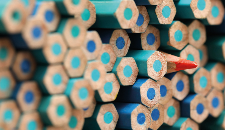 A single sharp orange colored pencil pointing in the opposite direction to the large quantity of blue pencils. Standing out in the crowd or being different concept. Individuality