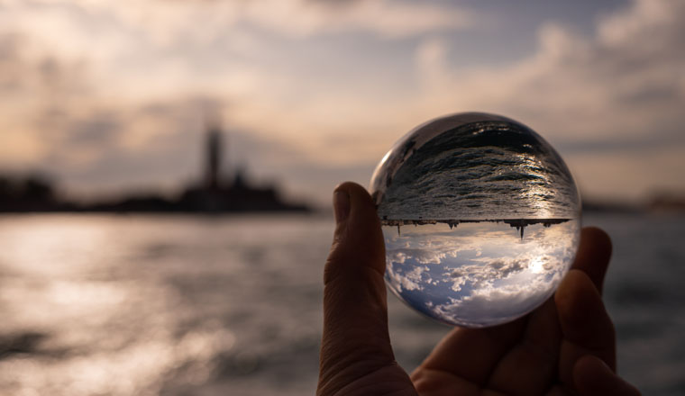 Hand holding glass sphere in front of sunset in Venice (Italy), reflection in sea
